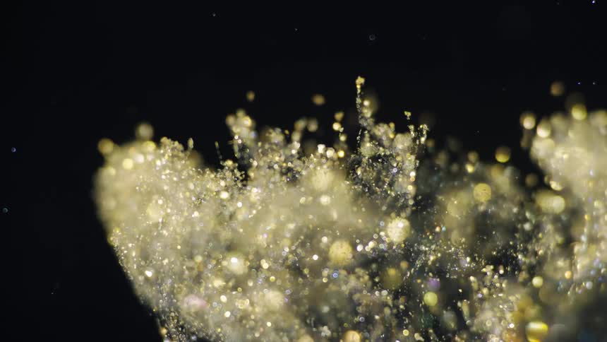 Crystalline particles fly up against black background glinting gold