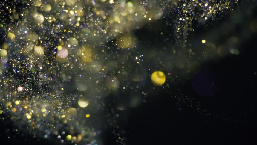 Golden light spots flicker over metallic glitter flowing through the dark