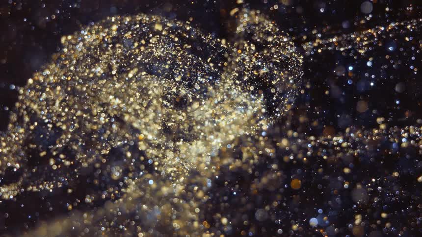 Gold glitter shimmers as it swirls across a dark background