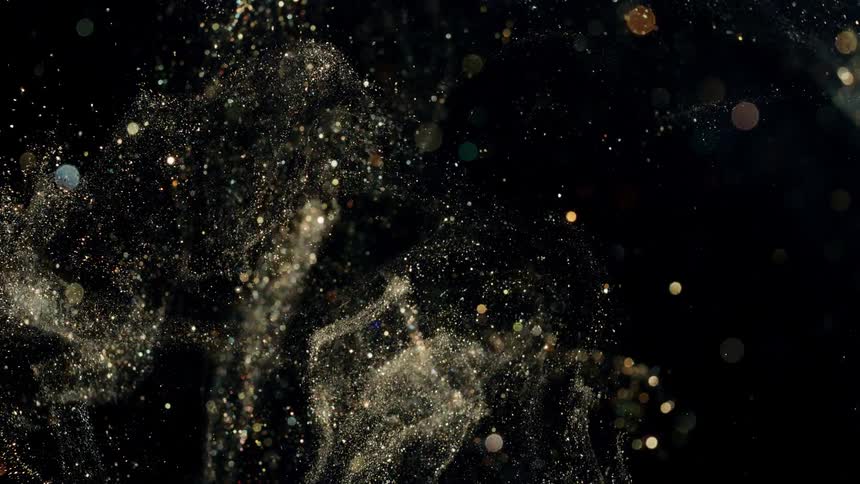 Golden glitter is tossed against a black background and moves in all directions