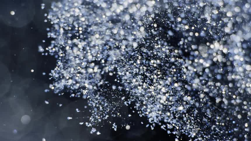 Blue and gold tinted crystalline particles fly through darkness