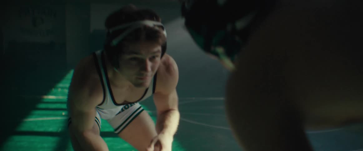A pair of wrestlers circle one another in a dimly lit gym during the day