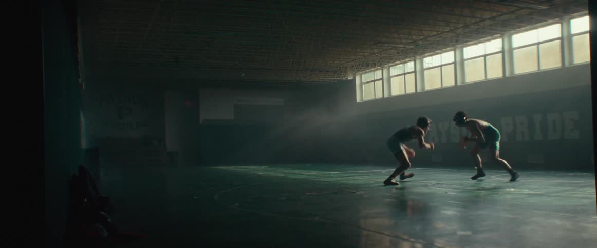 A pair of young wrestlers wrestle on a padded floor in a gym during the day