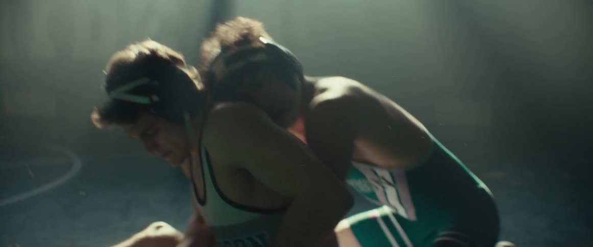 Two boys in wrestling uniforms grapple one another in the school gym