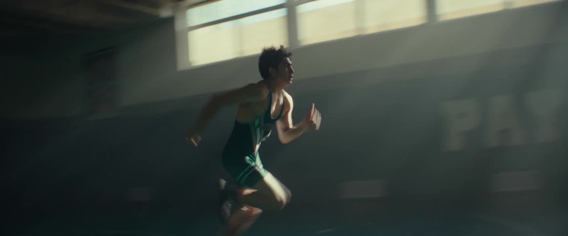 A young man sprinting across an empty sunlit gymnasium