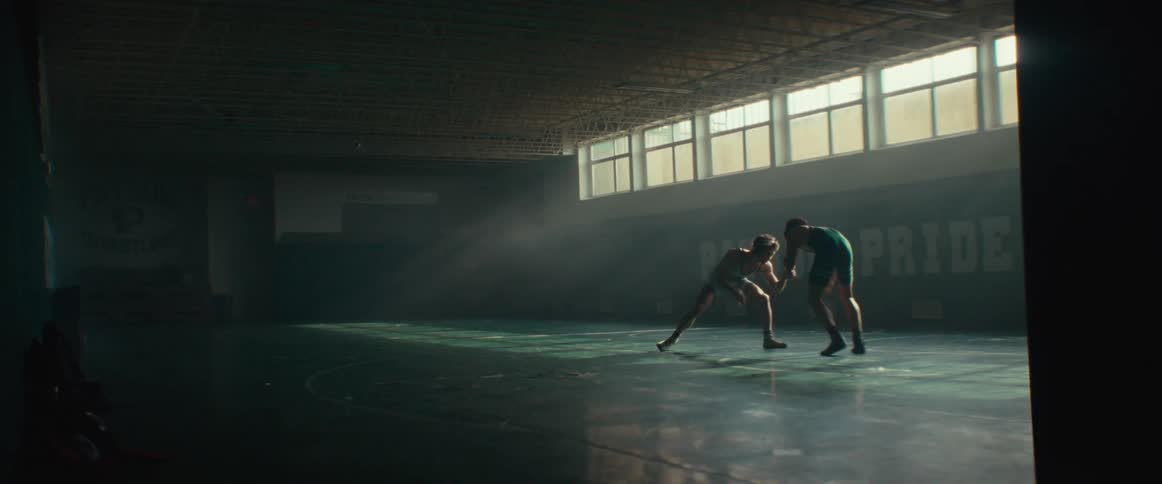 Two men wrestle in a dimly lit room