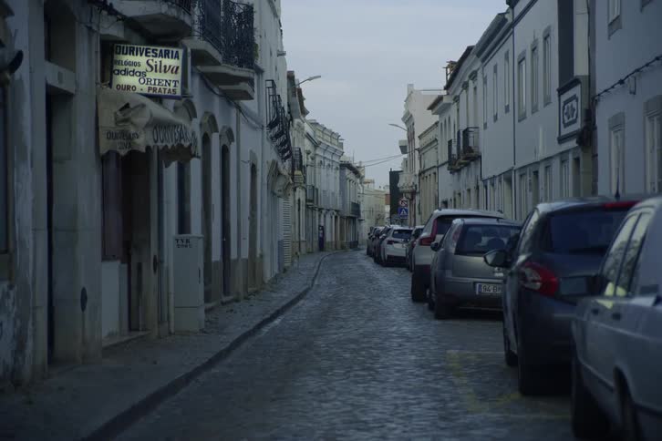 A line of vehicles parked along a narrow street in a city during the day