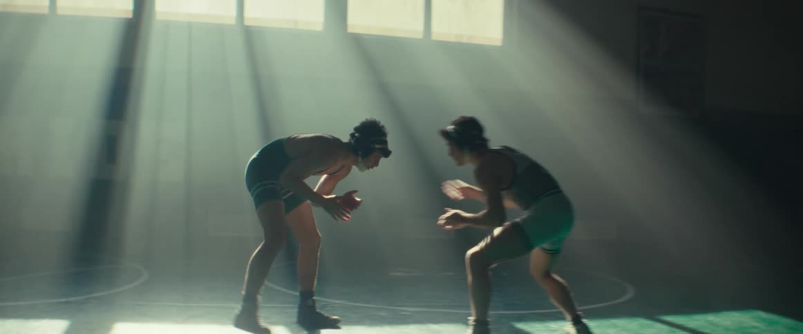 A pair of young men wrestle in a dimly lit gym during the day