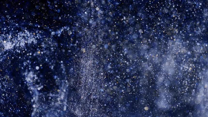 Crystalline particles fly through darkness sparkling and creating light spots