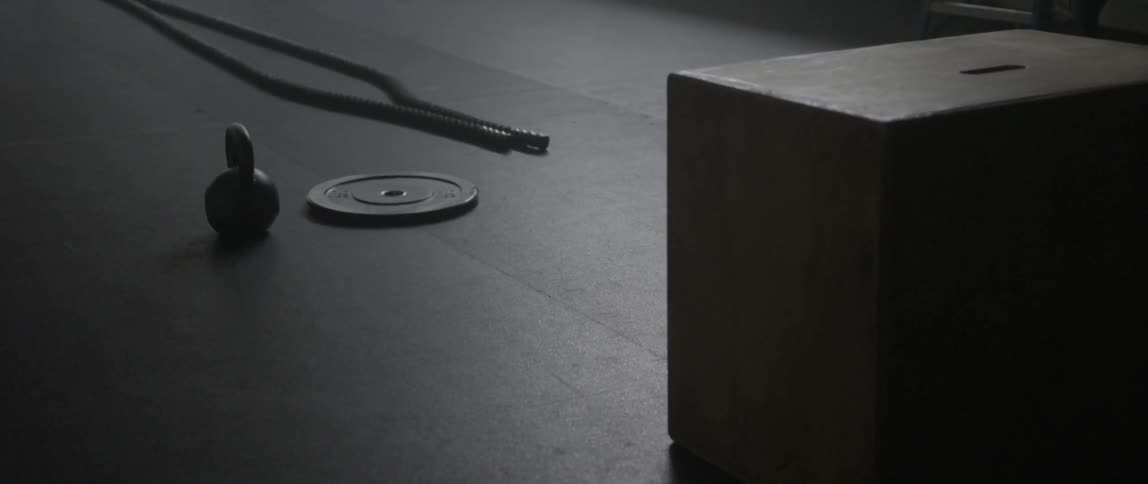 A weight plate, rope, and kettle bell are on the ground of a gym