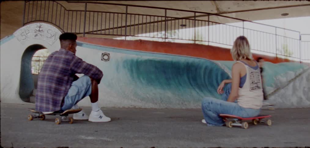 A man executing a skate trick on his skateboard at the skate lane while his friends are watching while seated on their skateboards