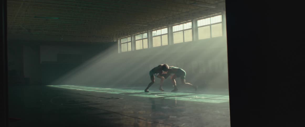 Two young men wearing wrestling clothes wrestling on an empty gymnasium