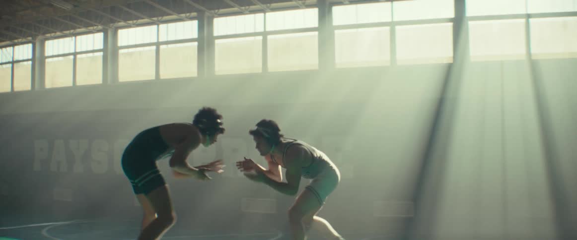 Two athletes wrestle in gym lit from high windows