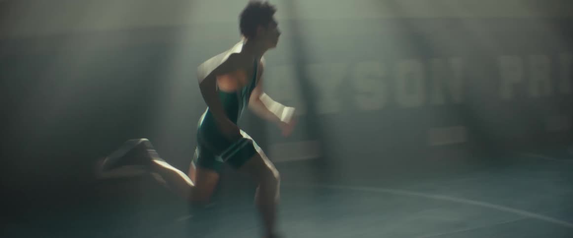 A teenage wrestler runs through the light in the school gym and into darkness