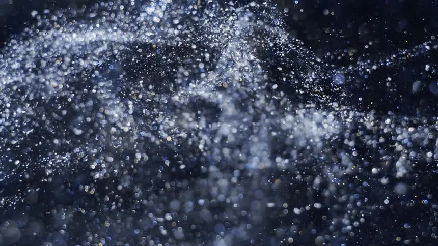 Pale particles flow in flurry against black background