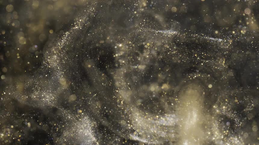 Mass of pale golden particles swirls and glints against black background