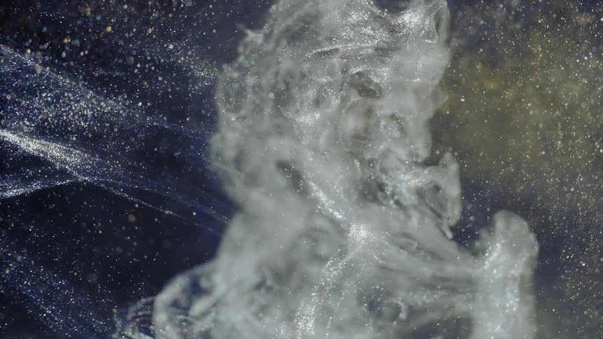 Glitter is moving through the air while a billowy cloud of smoke is introduced to it from the right