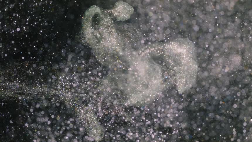 Pale layer of glinting particles flows through white spots on black