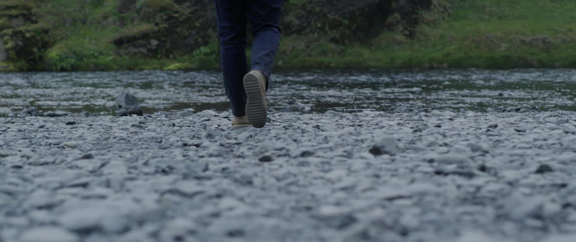 Man is walking across rock beach towards flowing river