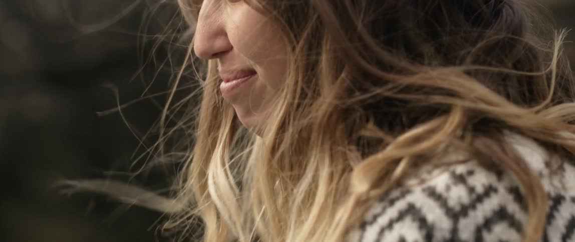 A woman is smiling as the wind blows her hair while she stands outside in daylight
