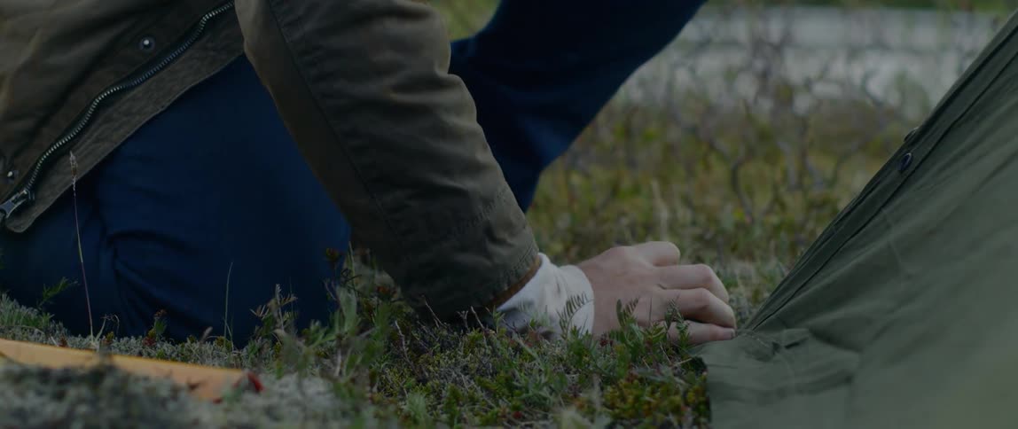 A man uses a rock to hammer a stake into the ground to hold down a tent