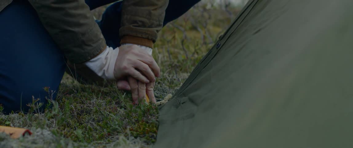 A man puts a stake in the ground to secure a tent