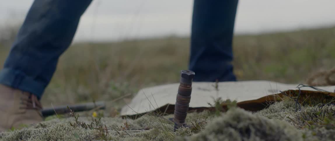 A person stabbing a knife into the earth before walking off