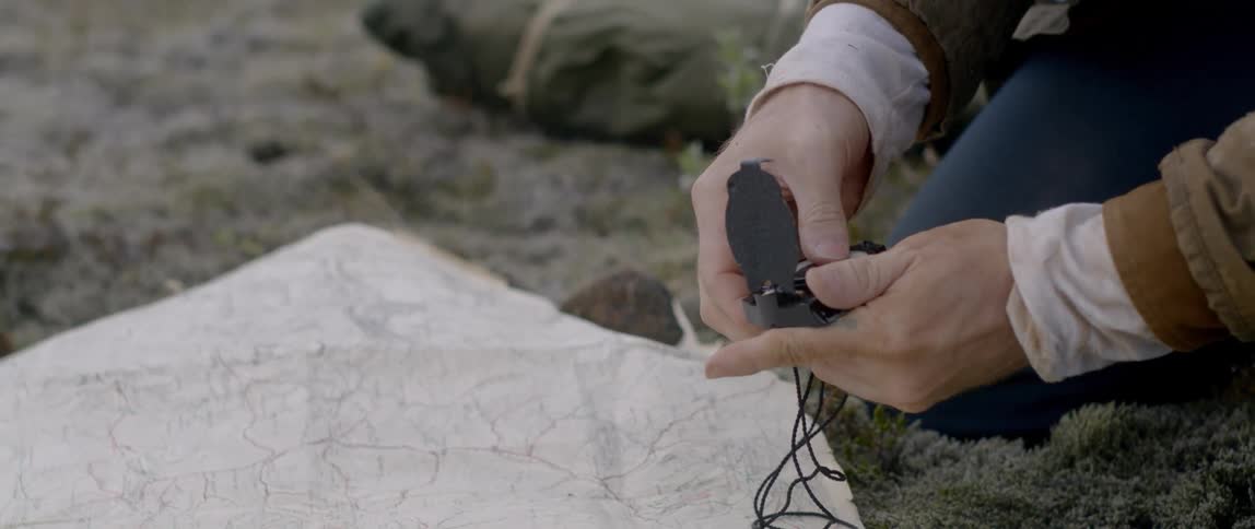 An adult male opening a compass and placing it on top of a white stone in a mossy area outdoors