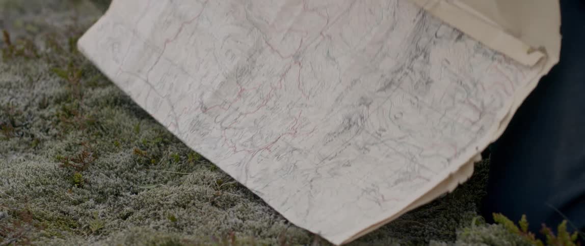 A man kneeling on the ground opens up a map