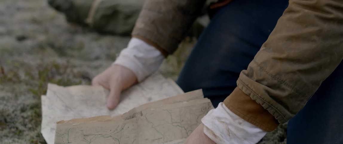 A man knees on the ground and unfolds a map
