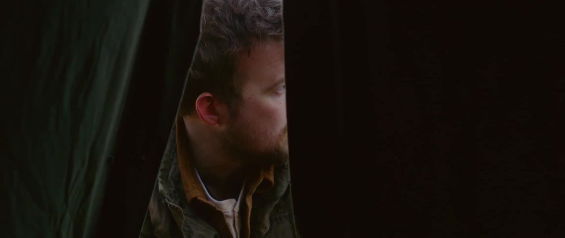 A young man looks around worried outside of a tent