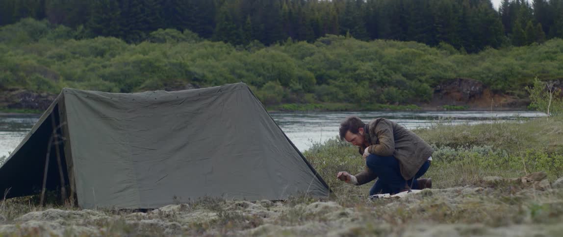 A man secures a tent on land near a river
