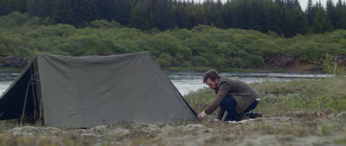 Ma adjusting a tent outdoors near a stream
