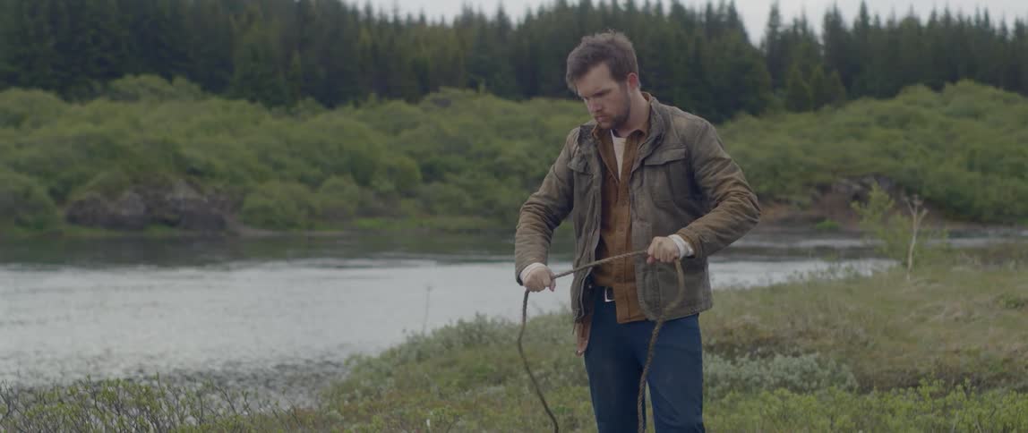 A man gathers a rope in his hand standing beside a lake