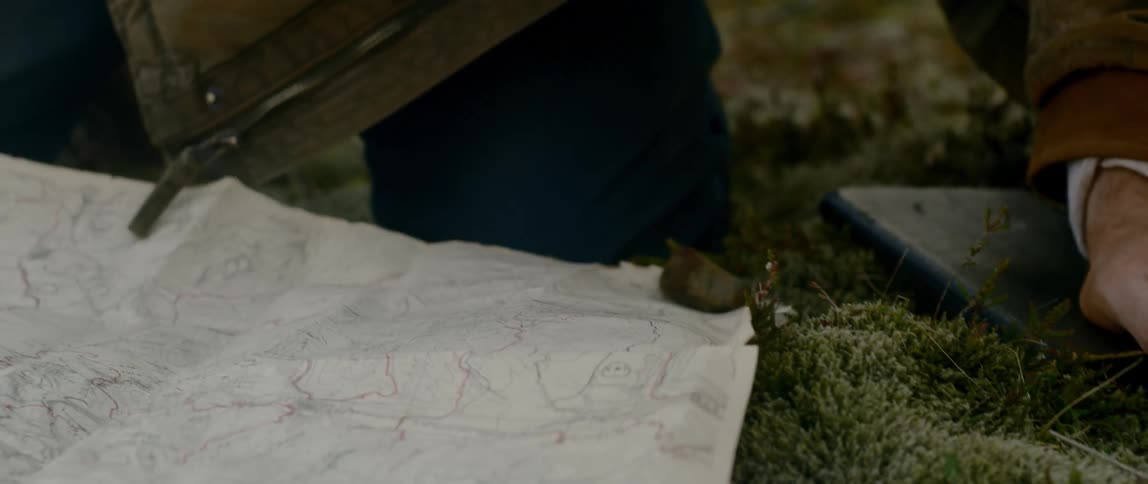 A man using rocks to hold a map still on the ground
