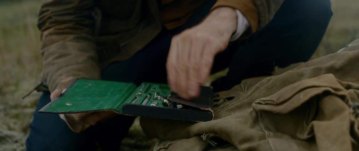 Man opening a box contain some stainless tools in the middle of a grassland