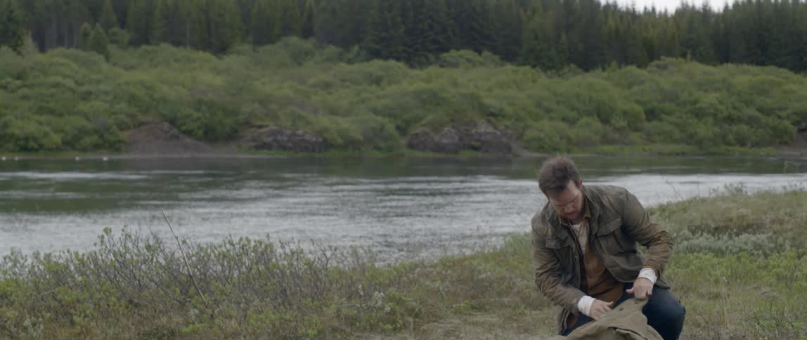 A man in front of a river taking a book out of a backpack