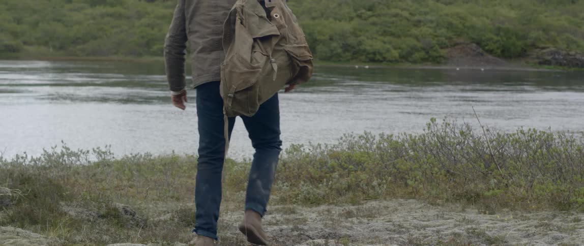 A man with a backpack walks over to a lake