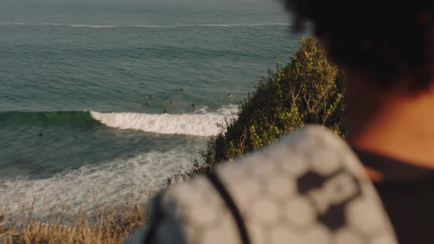 Young woman on a hill watching people surf in the sunny sea