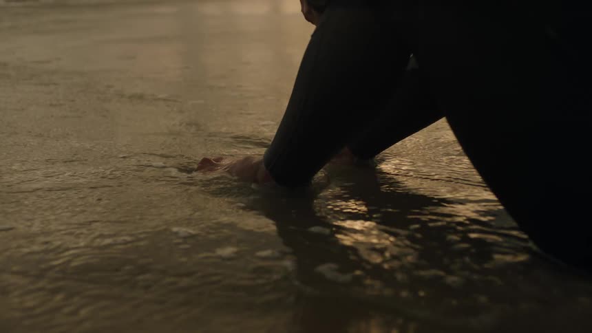 A person sitting at the waters edge on the beach with the water gently flowing over their feet