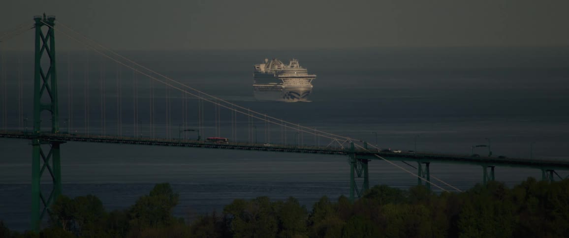 White cruise ship moves toward coast near busy suspension bridge