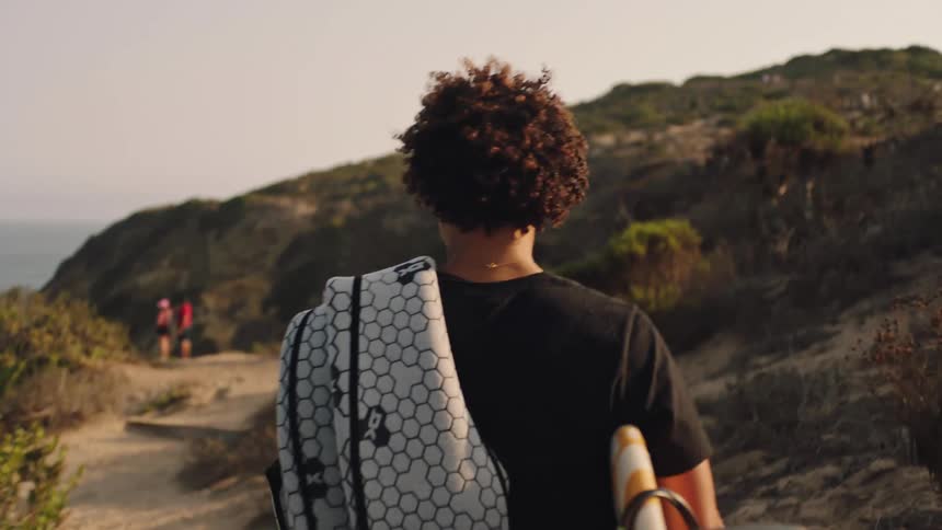 The backside of a person walking down a trail near the ocean on a coastal path