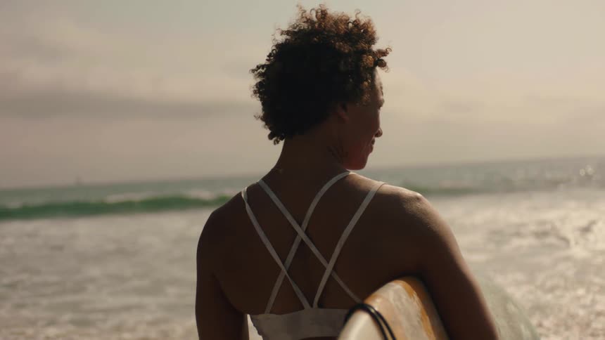 A woman stands on the shore with a surfboard
