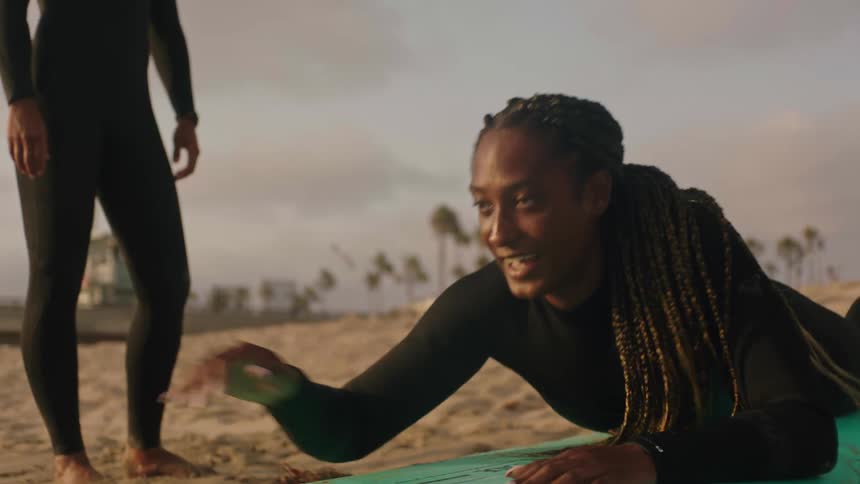 Experienced surfer lies on surfboard on beach teaching another person how to paddle