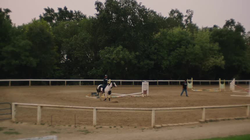 A horseback rider leads the horse around the arena while the trainer walks towards them