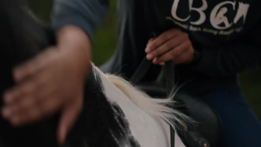 A woman strokes the neck of a horse while sitting in its saddle during the day