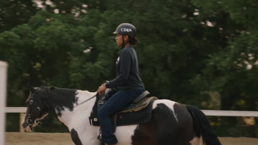 A woman slowly rides a horse around an enclosure during the day