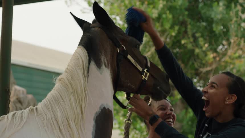 Two women laugh while brushing their horse
