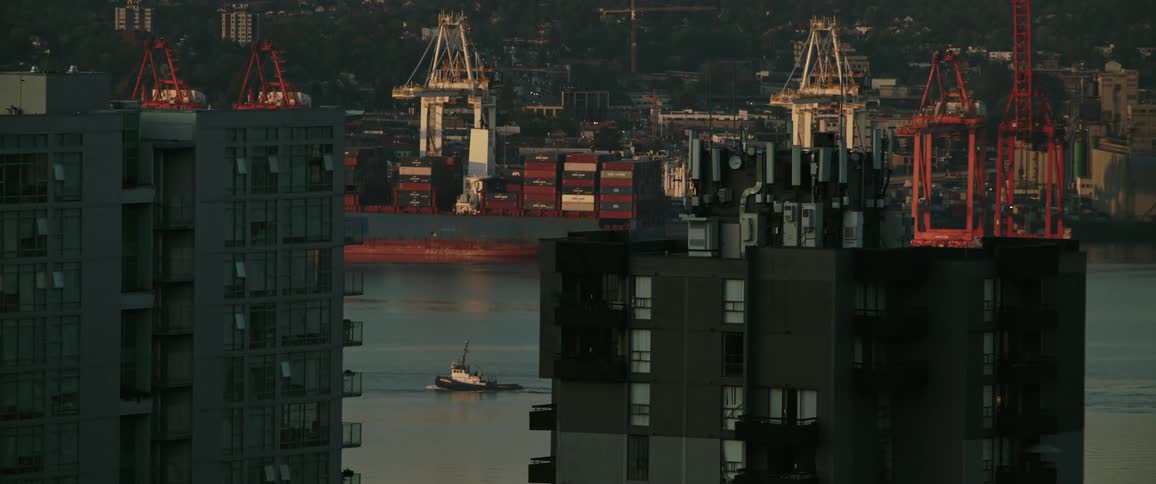 Wide shot of a city with construction cranes and equipment near the waters edge as a boat travels by