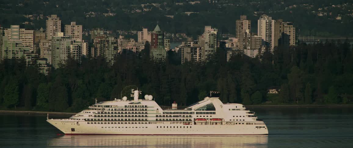 A ship is driving on a body of water outside of a city